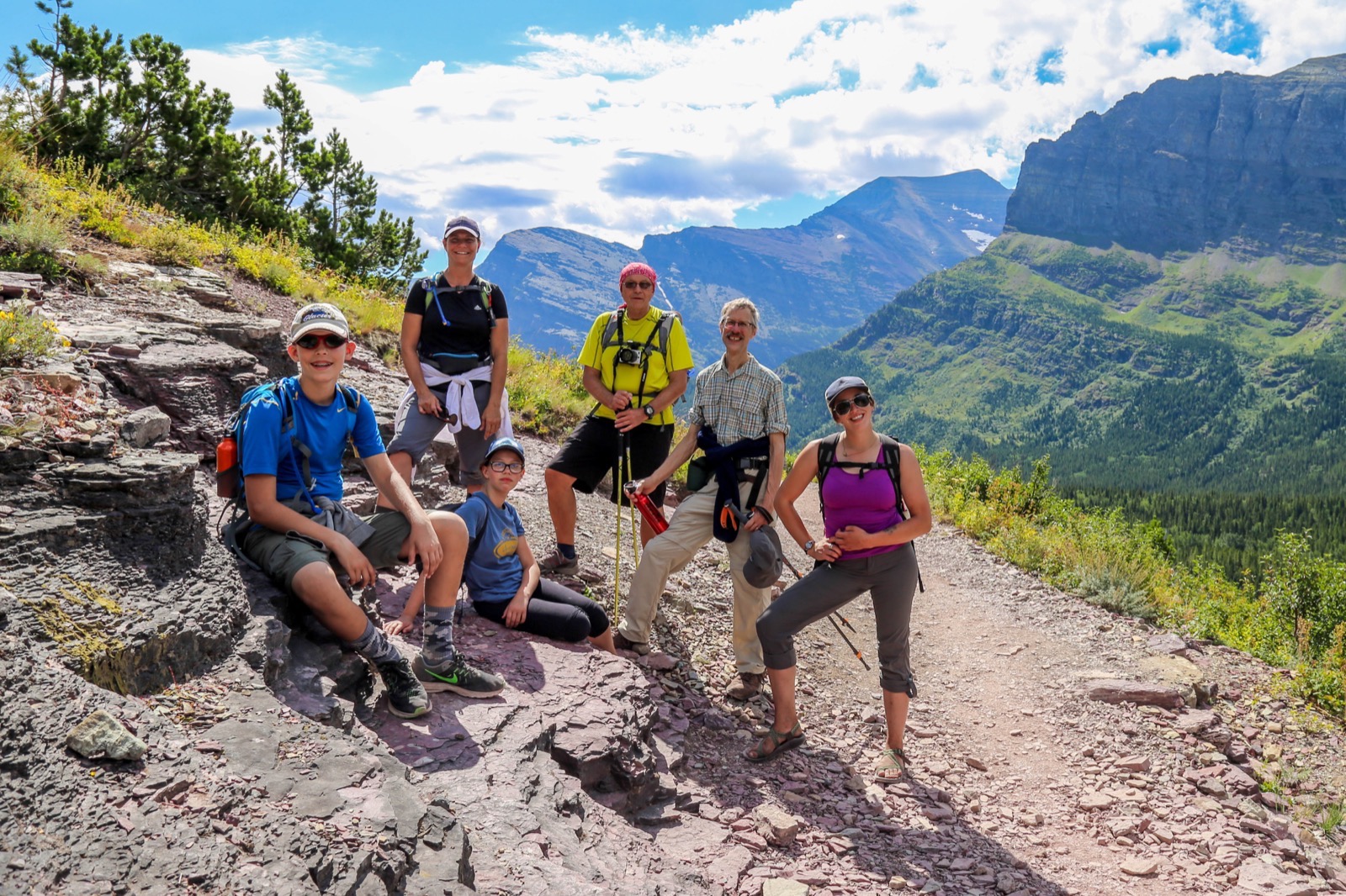 Family takes a break from hiking to pose in front of massive valley in Glacier National Park.